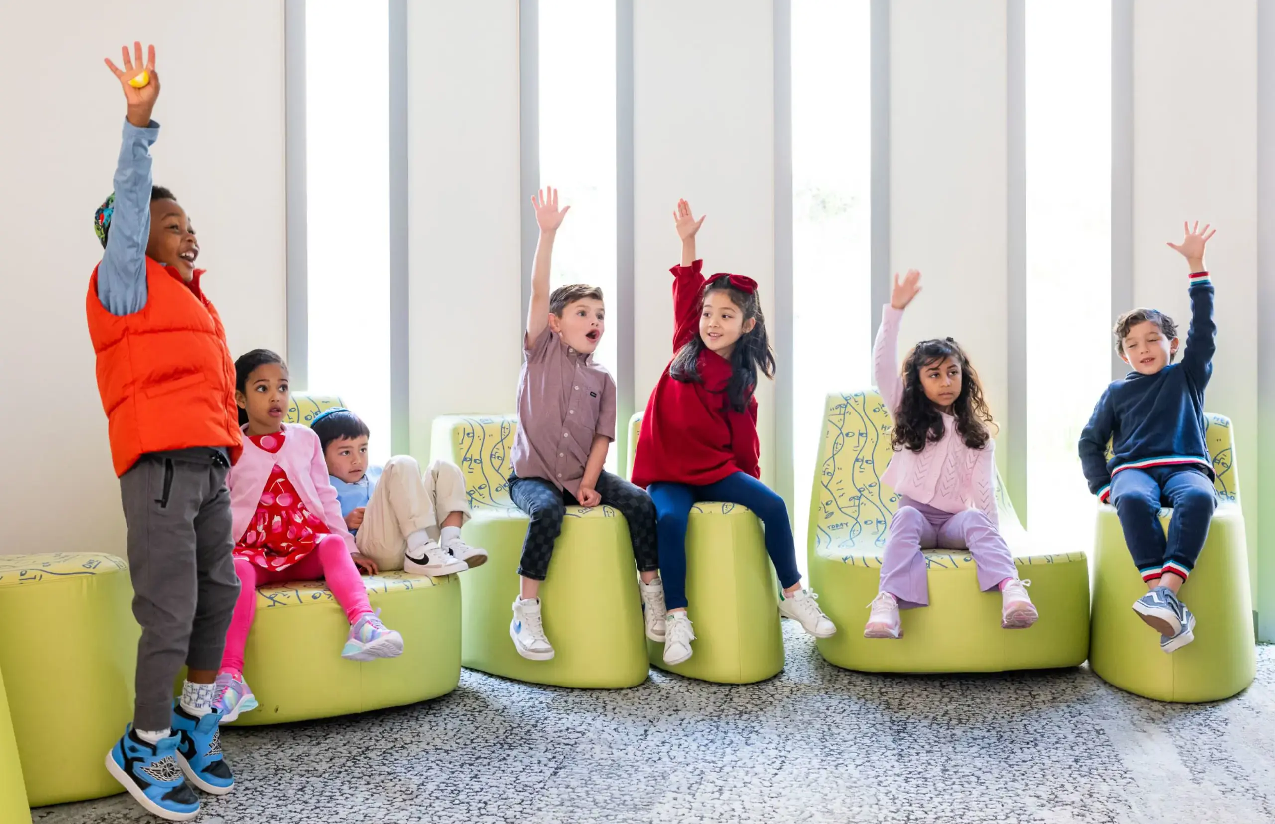 Students sitting on green chairs, raising their hands